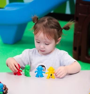 Child with pigtails playing with colorful toy figures on a table at a playspace.