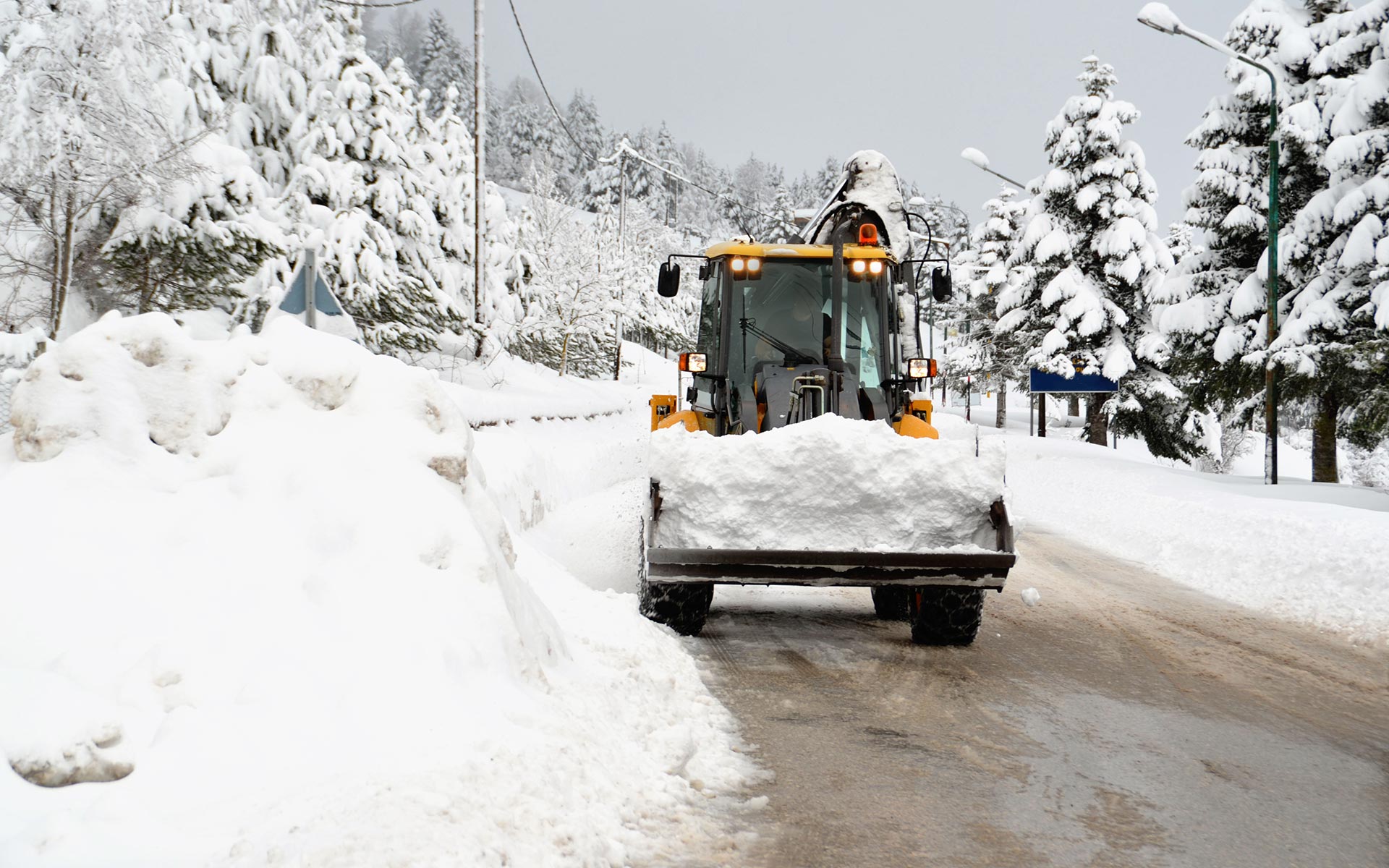 A snow plow is driving down a snow covered road