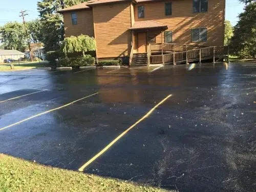 Paved parking lot in front of a two-story brown building with a ramp, yellow parking lines, and green grass.