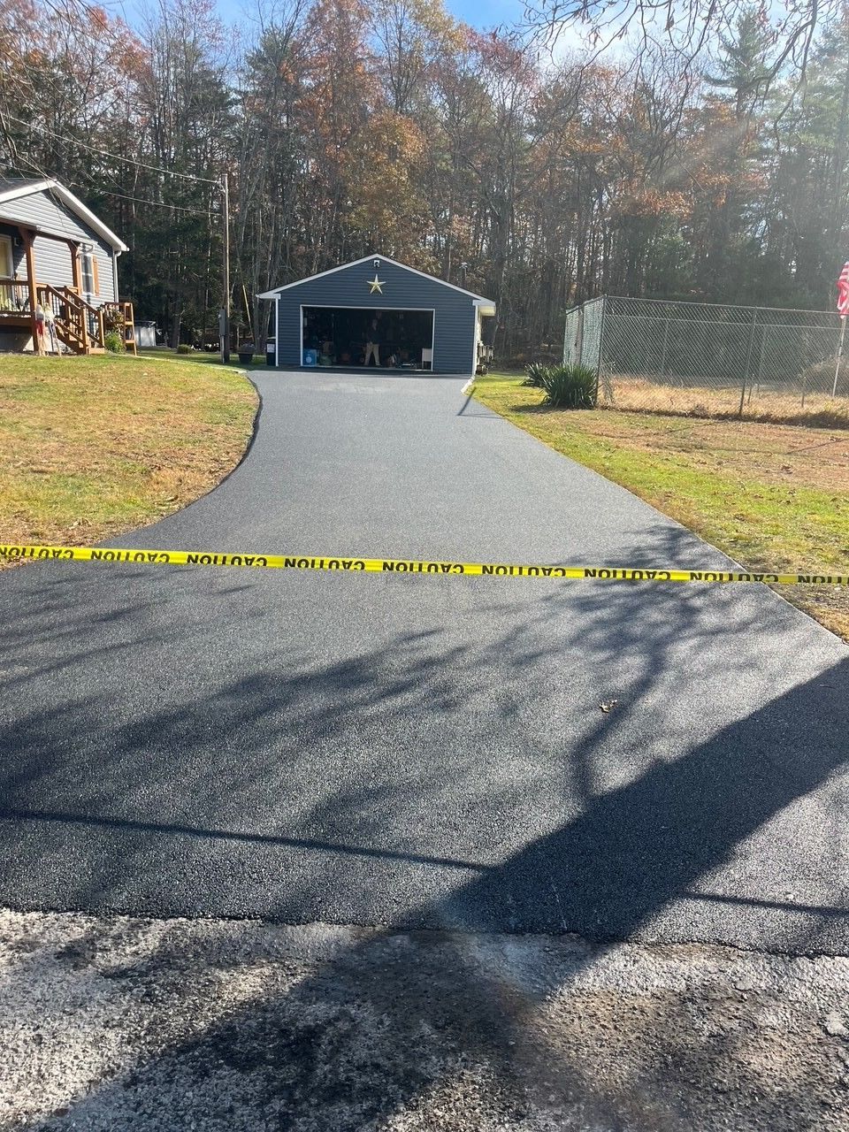 Freshly paved asphalt driveway leading to a blue garage, yellow caution tape across the entrance.
