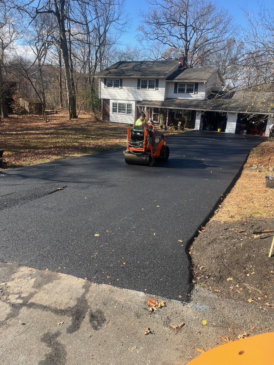 Asphalt driveway being rolled by a small construction machine in front of a house.