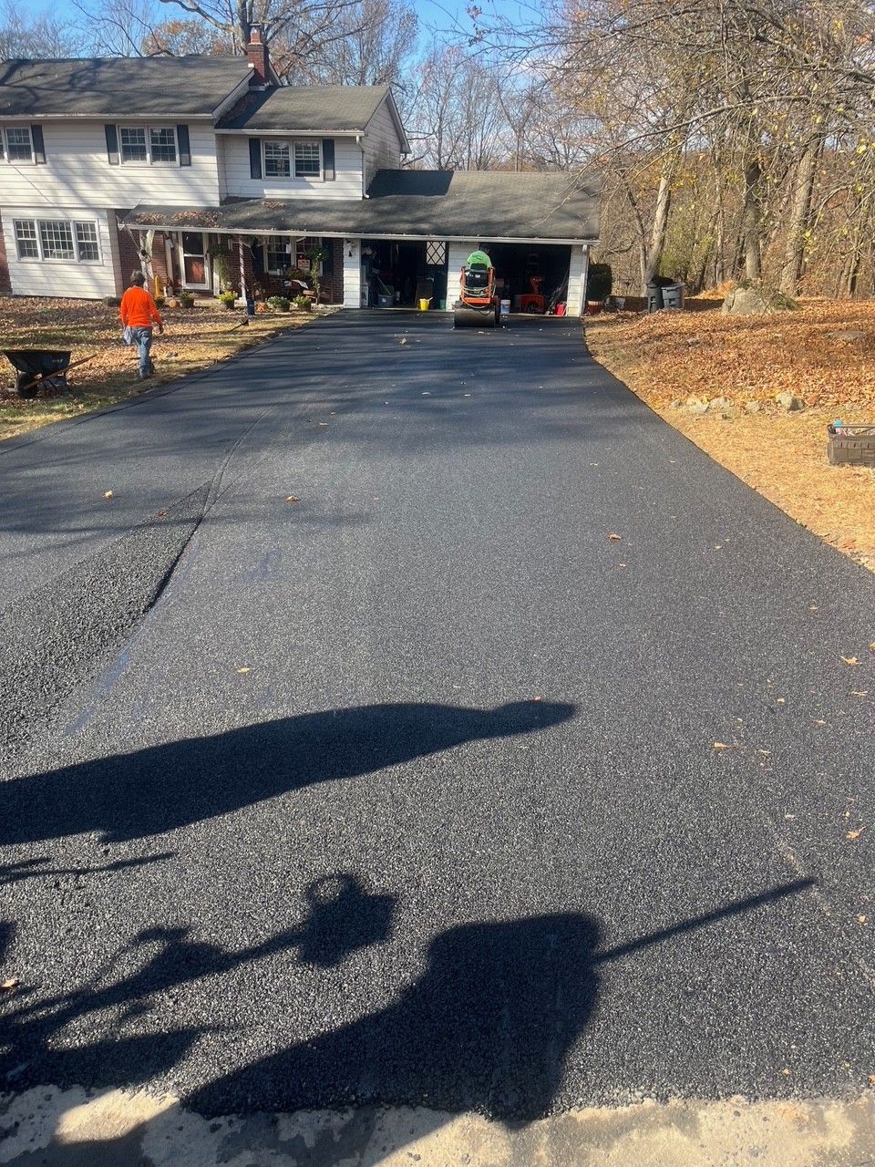 Newly paved asphalt driveway leading to a two-story house with a garage.