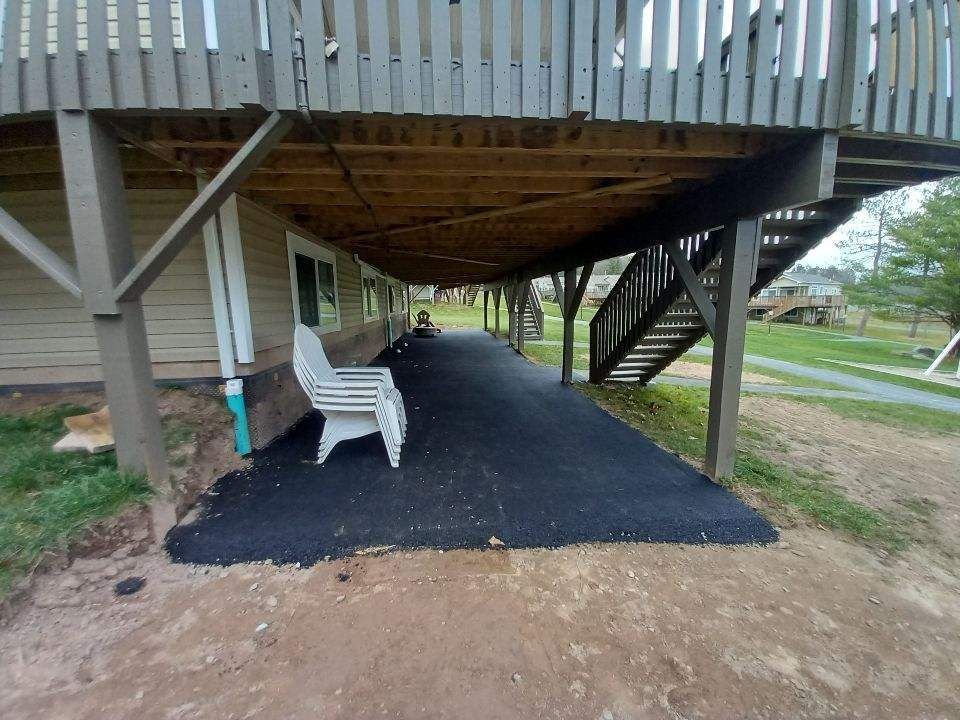 Asphalt walkway under a deck with white chair; brown framing and stairs.