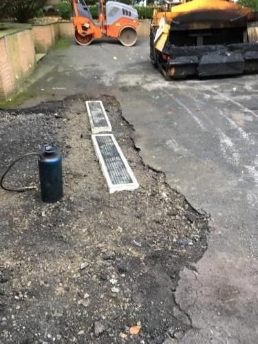 Road repair: Asphalt removed, propane tank, grates, roller, and asphalt paver on a road.