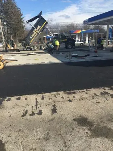 Asphalt paving at a gas station. Workers, dump truck, and machinery on a sunny day.