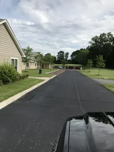 Blacktop driveway leads past tan buildings and green grass under cloudy sky.