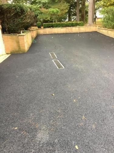 Asphalt driveway with rectangular drain, bordered by brick and greenery.