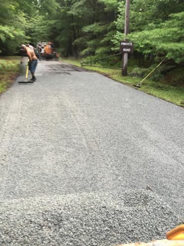 Man raking gravel on a road. Forest in the background. Road sign visible.