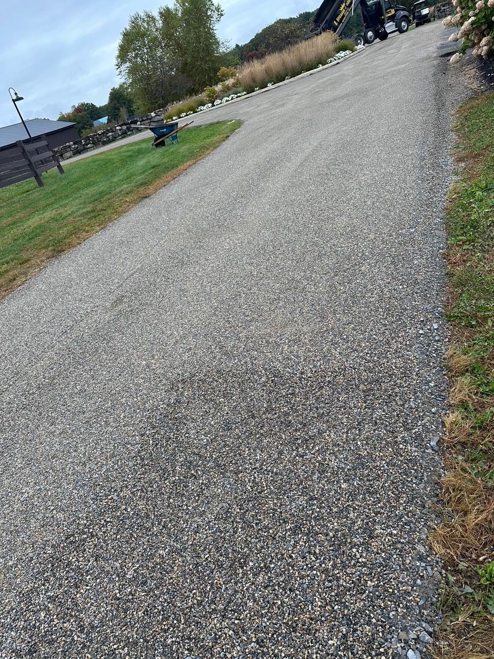 Gravel pathway curving through a green lawn, leading towards buildings and a clear sky.