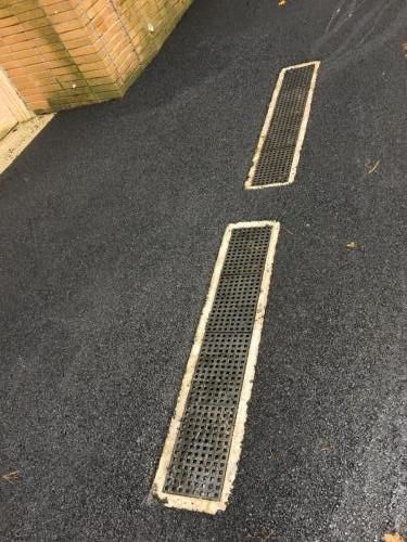 Two rectangular metal drain covers in asphalt.