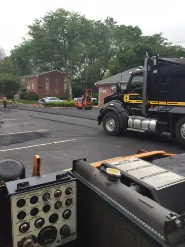 Asphalt paving in progress: truck, forklift, and workers on site.