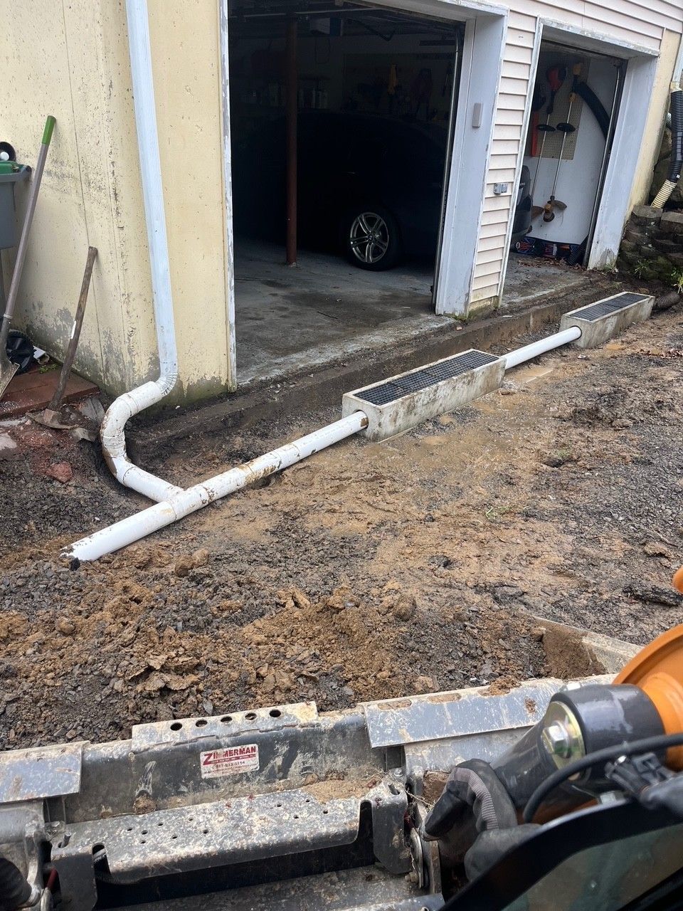 Drainage system installation in front of a garage, with PVC pipes and concrete channels.