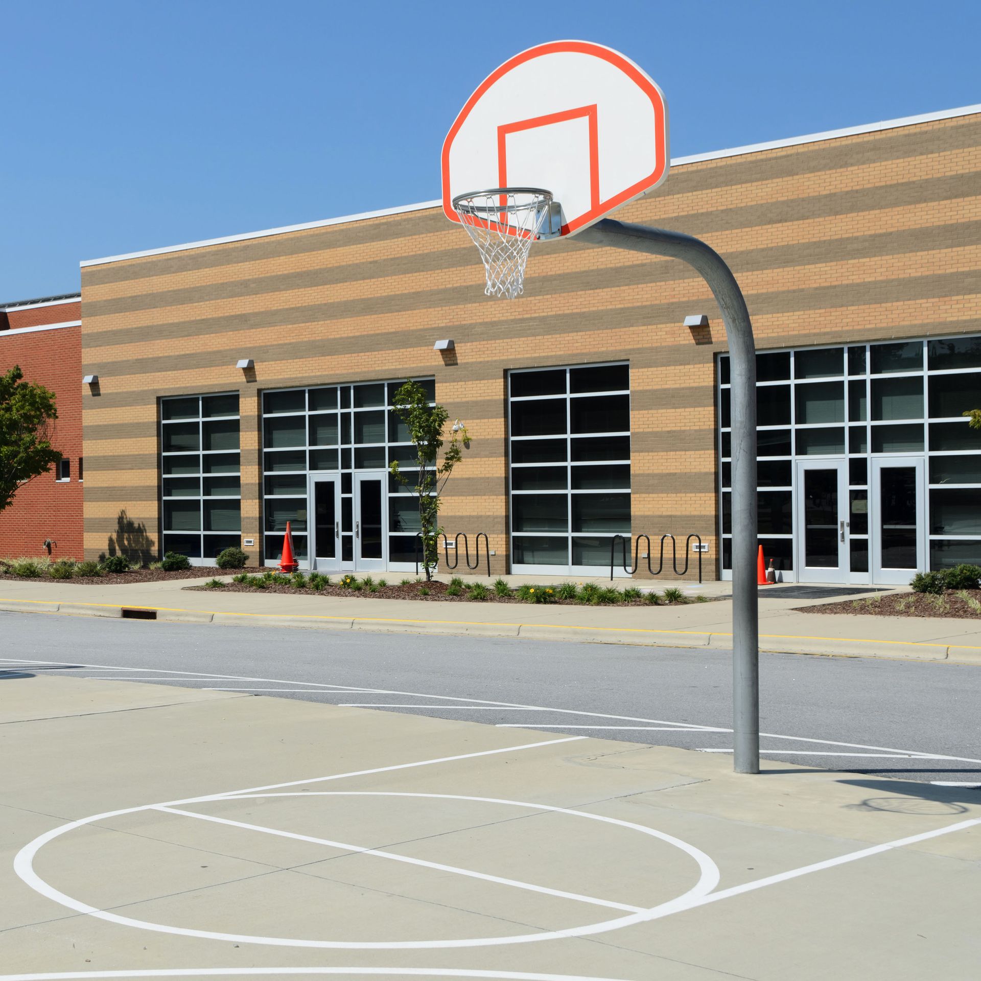 Basketball hoop on a concrete court in front of a school building.