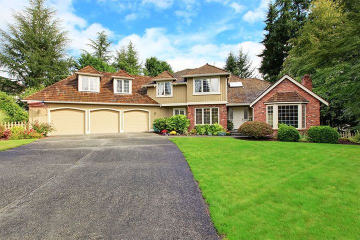 Suburban house with a three-car garage, brick facade, and lush green lawn under a bright blue sky.