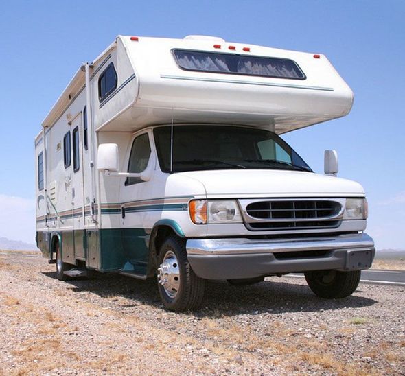 A white and green RV is parked on a dirt road.