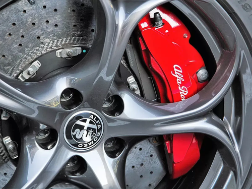 Close-up of a gray alloy wheel with a red Alfa Romeo brake caliper and drilled brake rotor