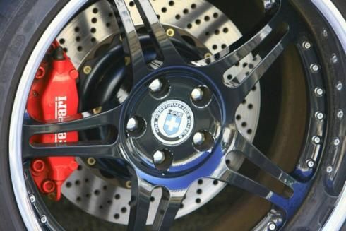Close-up of a custom car wheel with black spokes, silver drilled brake rotor, and red brake caliper