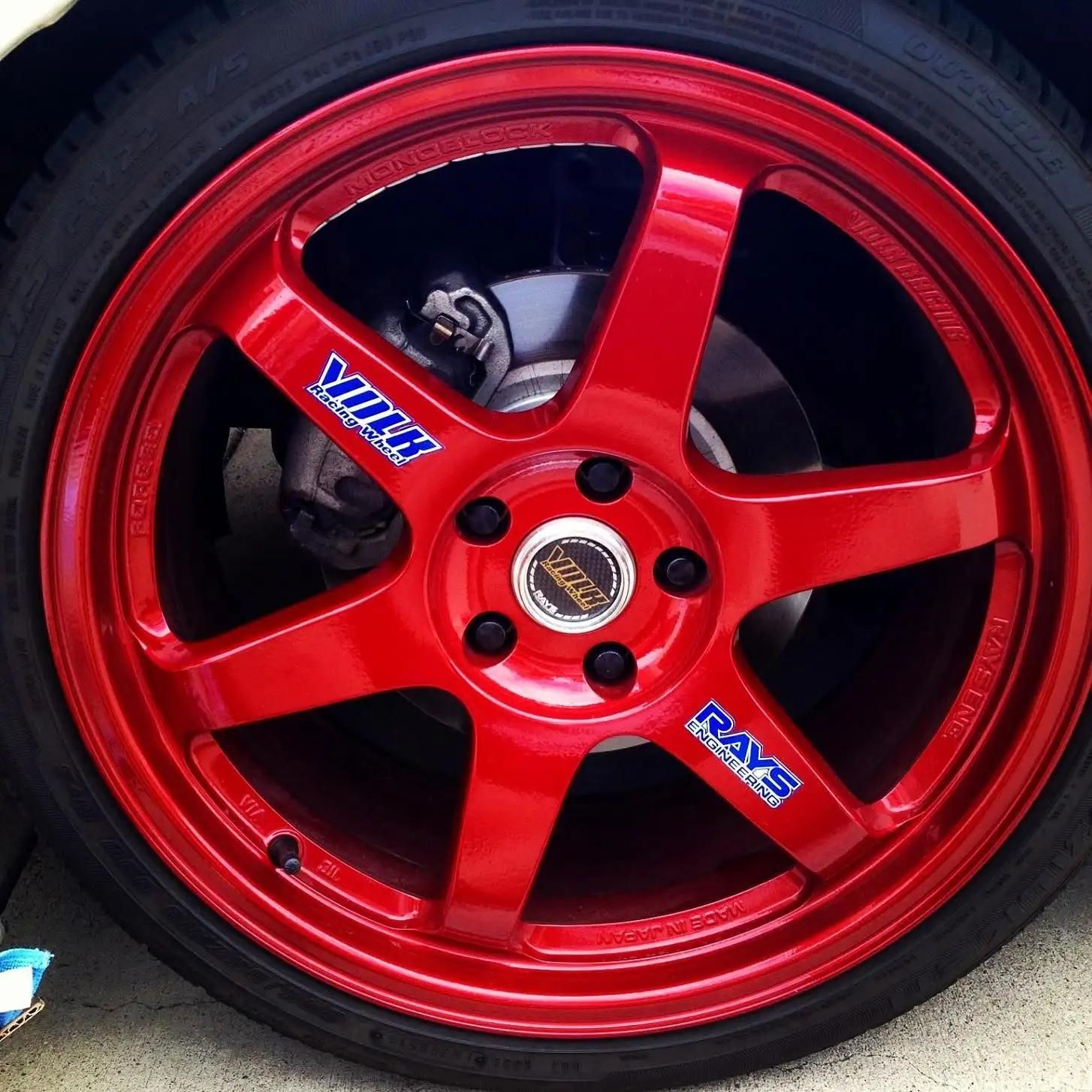 Red alloy car wheel with five spokes and brake caliper visible behind it