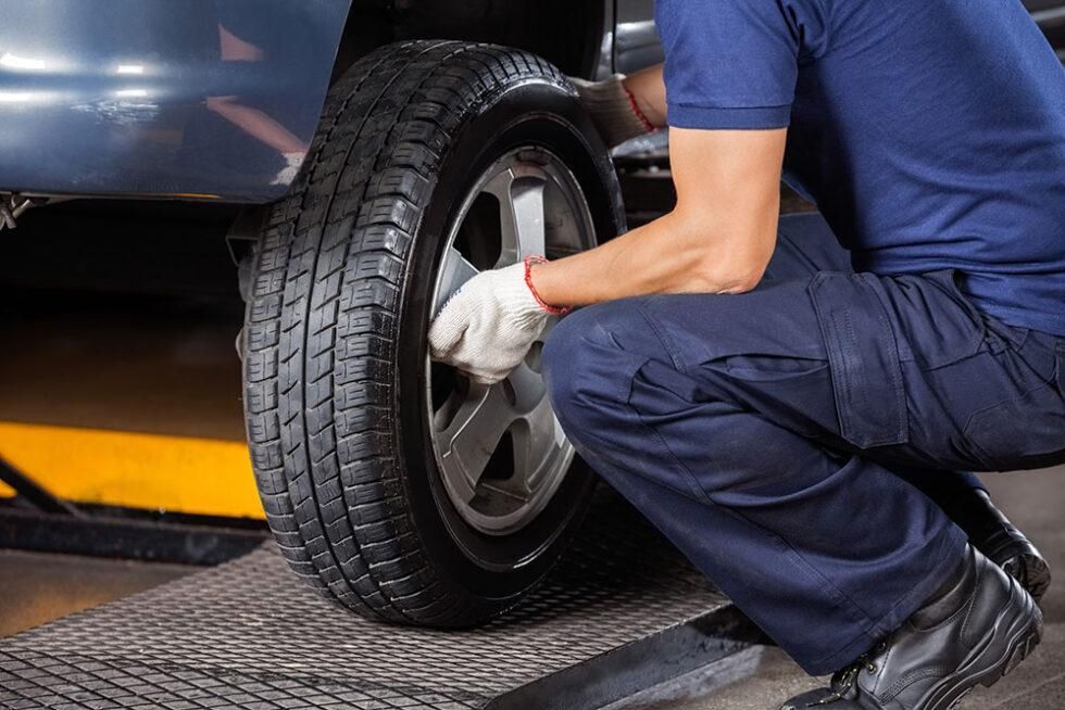 Mechanic crouching by a car wheel, tightening lug nuts with a tool in a garage