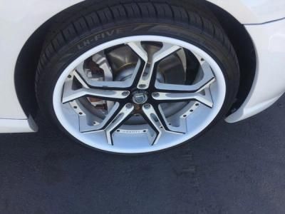 Close-up of a white car’s front wheel with a silver alloy rim on asphalt.