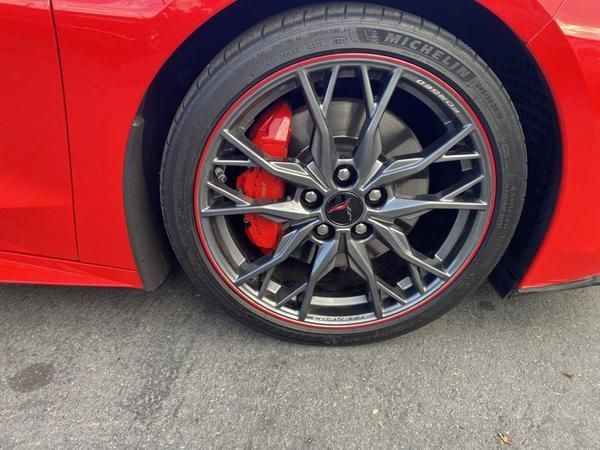 Red sports car wheel with black alloy rim and red brake caliper on pavement