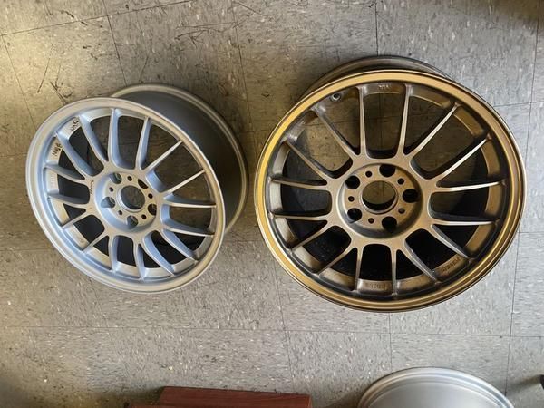 Two alloy car wheels: one silver and one gold, resting on a concrete floor.