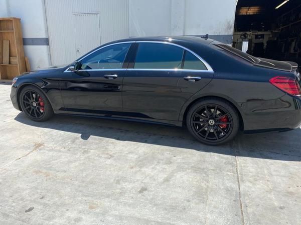 Black luxury sedan parked beside a warehouse, side view on a concrete lot