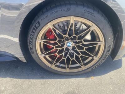 Close-up of a BMW wheel with black alloy rim, red brake caliper, and low-profile tire on a gray car.