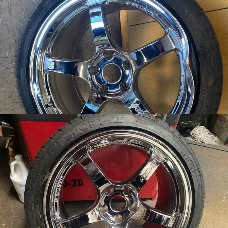Two chrome car rims stacked with a black tire in front of a red surface