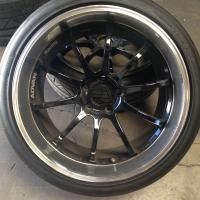 Close-up of a black multi-spoke car wheel rim with a polished chrome outer lip on a concrete floor