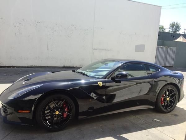 Black Ferrari sports car parked outdoors beside a white wall.