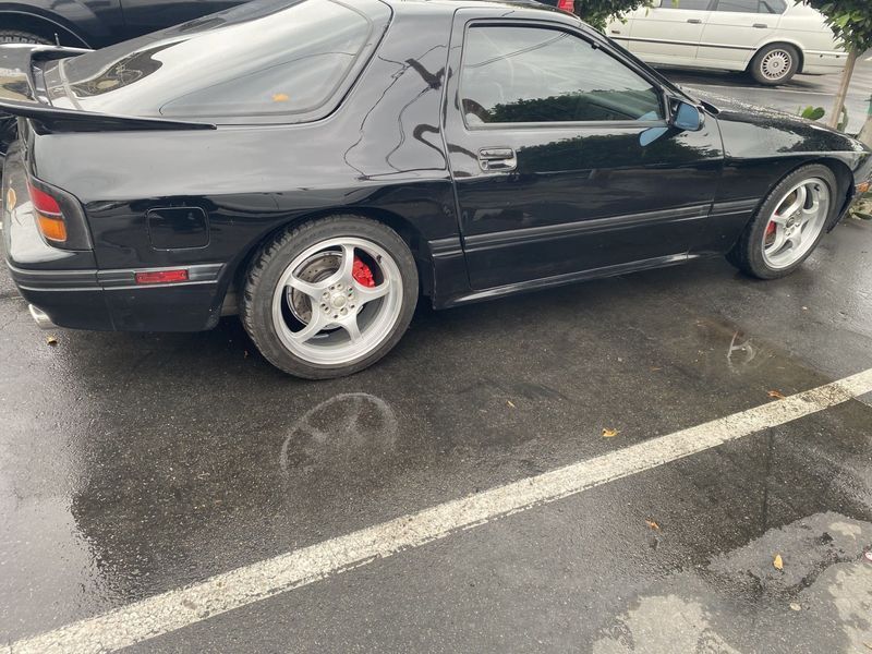 Black two-door coupe with silver rims parked in a wet lot over white parking lines