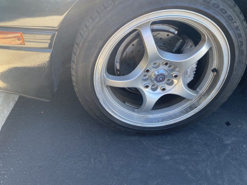 Low-profile car tire on a silver alloy wheel, seen close-up on a dark asphalt road.