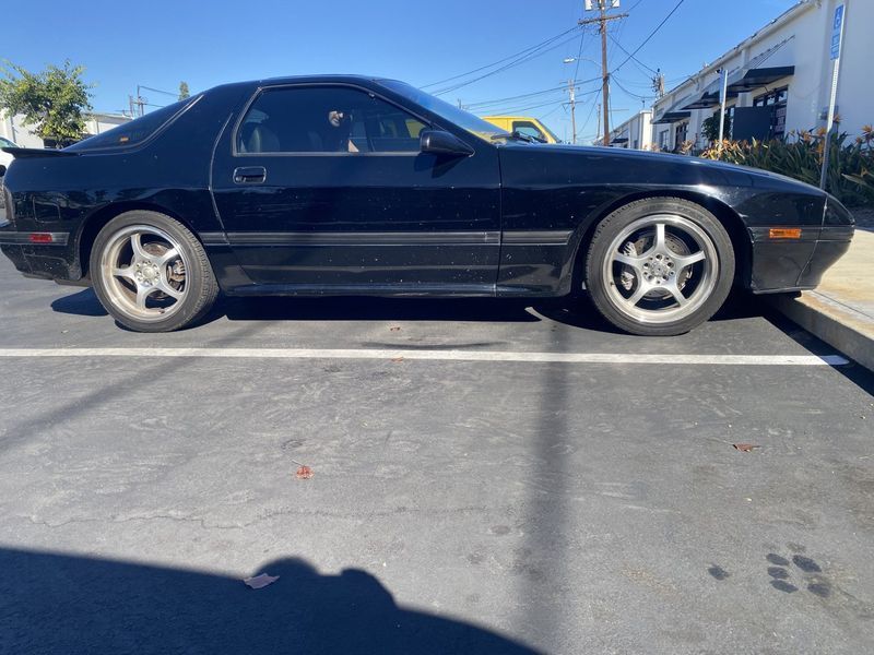 Black classic coupe parked in a lot under bright sunlight, side view.