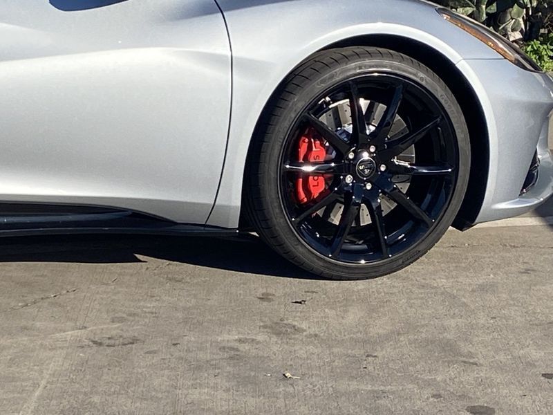 Silver sports car front wheel with black rim and red brake caliper, parked on pavement