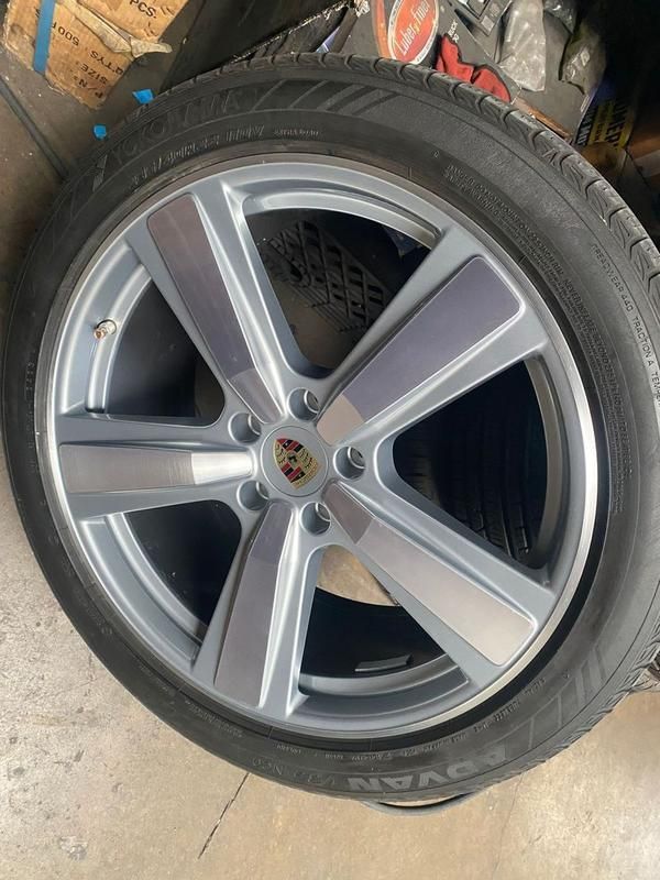 Close-up of a silver Porsche wheel with tire, shown in a garage or workshop.