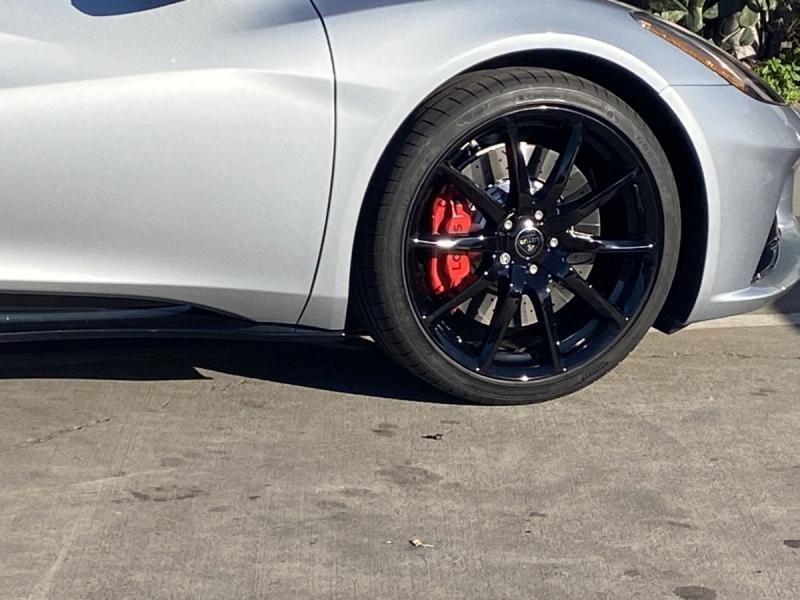 Silver sports car front wheel with black rim and red brake caliper on pavement