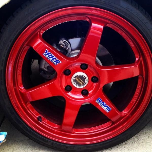Red 5-spoke car wheel rim with blue decals and brake caliper visible behind it.
