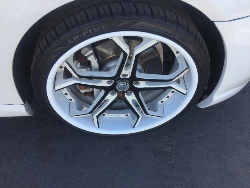 Close-up of a white car’s silver alloy wheel and tire on dark pavement