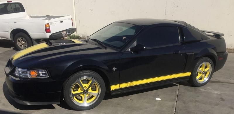 Black sports coupe with yellow trim and rims parked outdoors near a white pickup truck