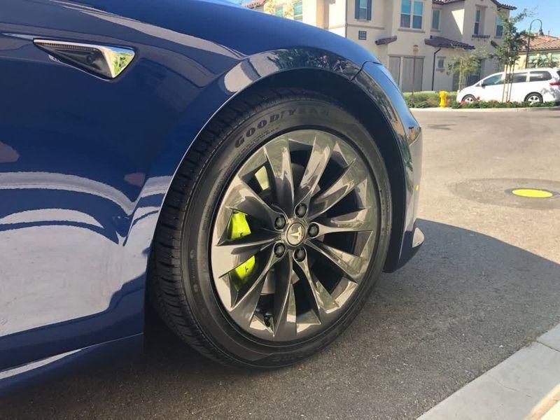Blue sports car wheel with black rim and neon yellow brake calipers on a sunny street