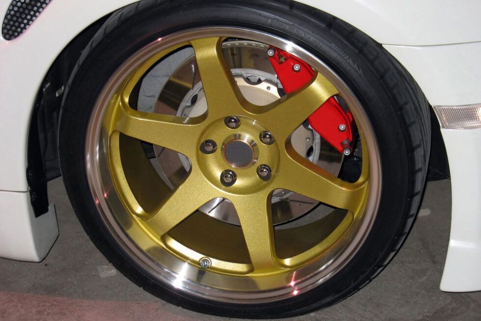 Gold alloy car wheel with a black tire and red brake caliper inside a white car wheel well