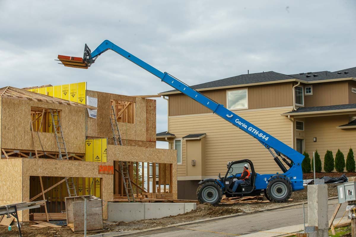 A man is driving a forklift over a house under construction.