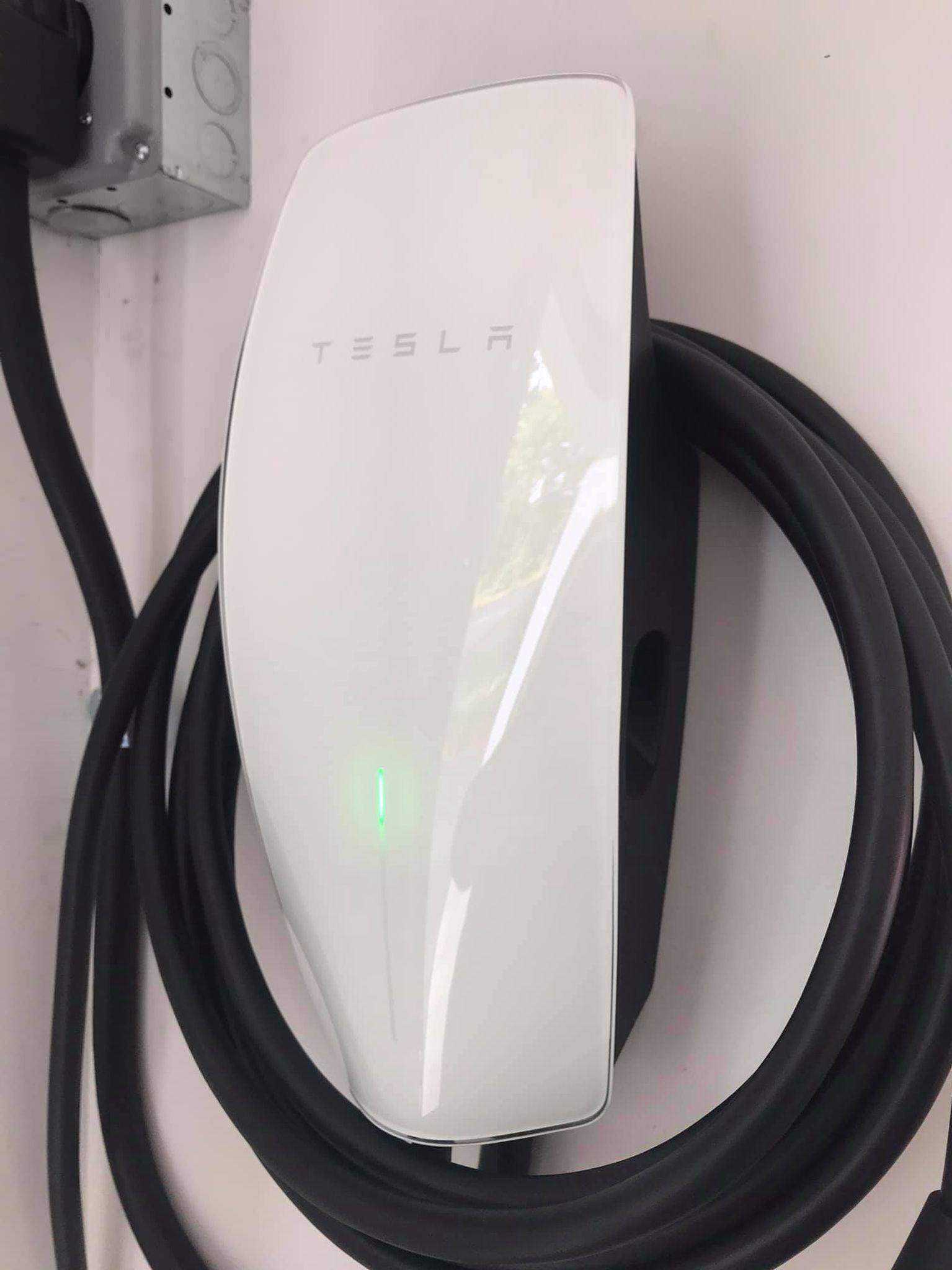 A white tesla charging station with a black cable attached to it