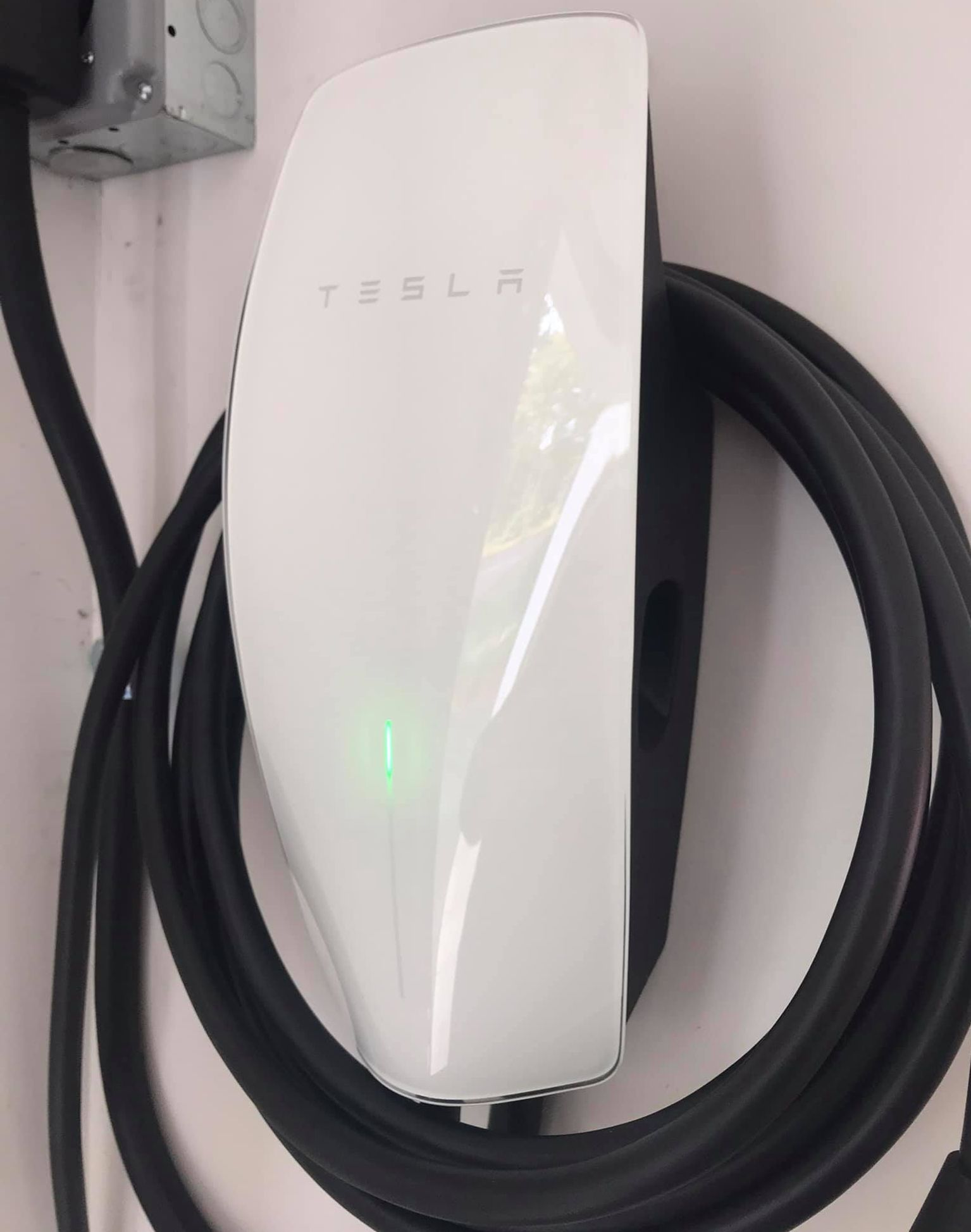 A white tesla charging station with a black cable attached to it