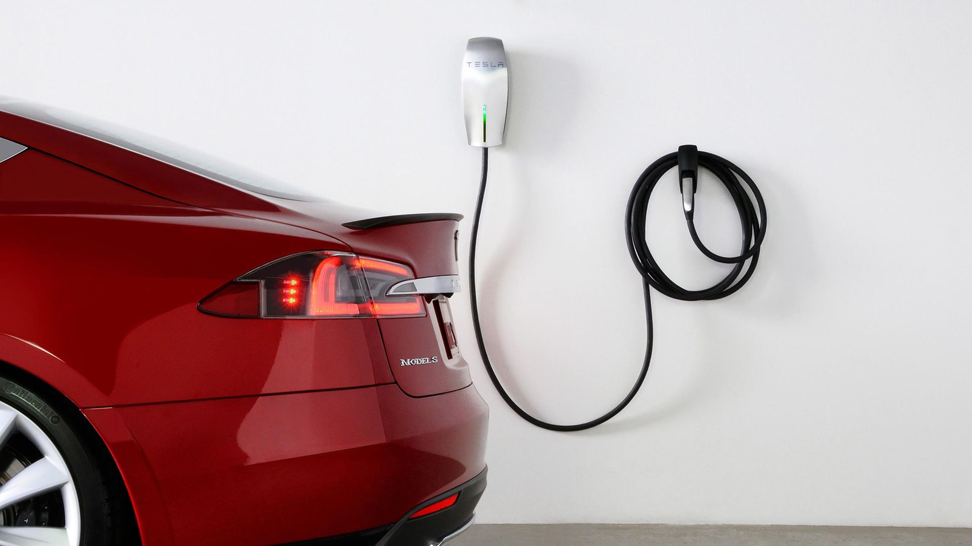 A red tesla model s is plugged into a charging station