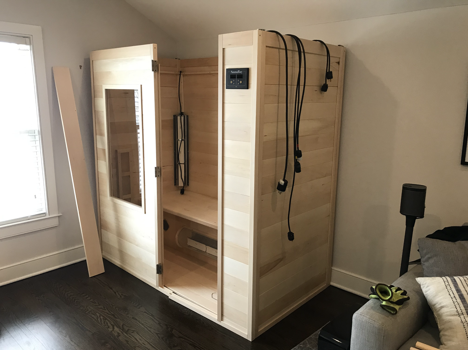 A wooden sauna is sitting in a living room next to a couch.