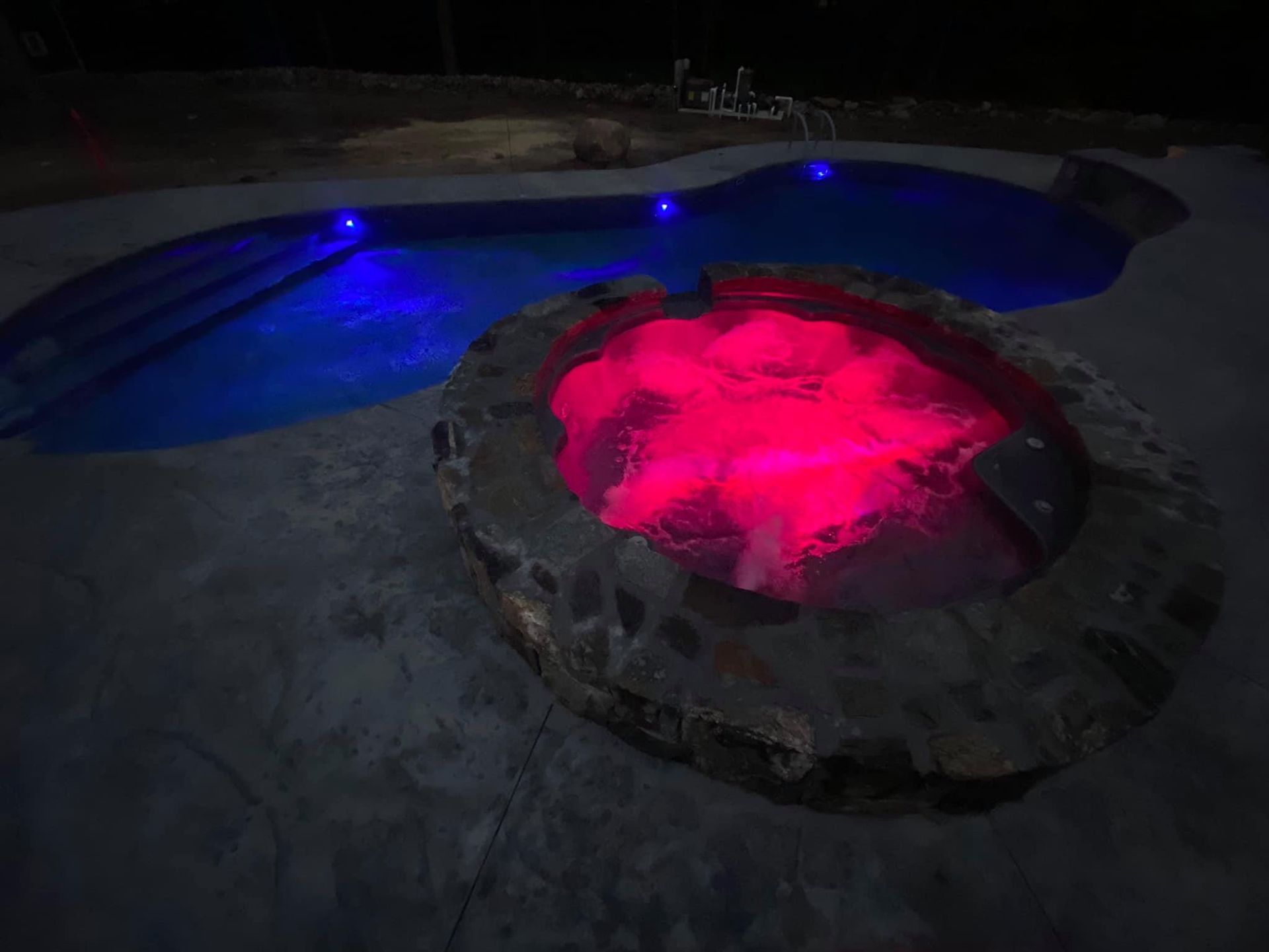 A hot tub is lit up at night next to a pool.