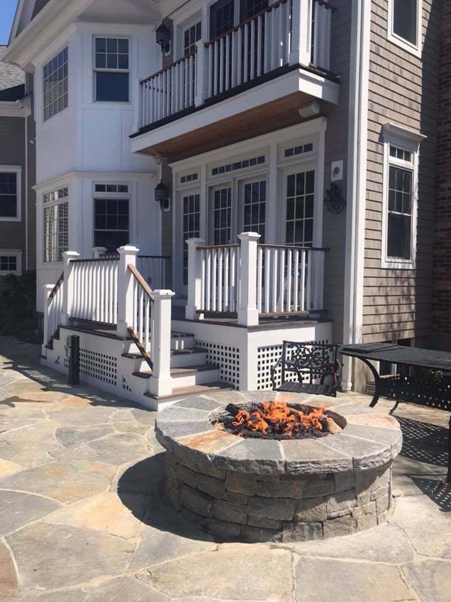 A fire pit is in front of a house with a balcony.