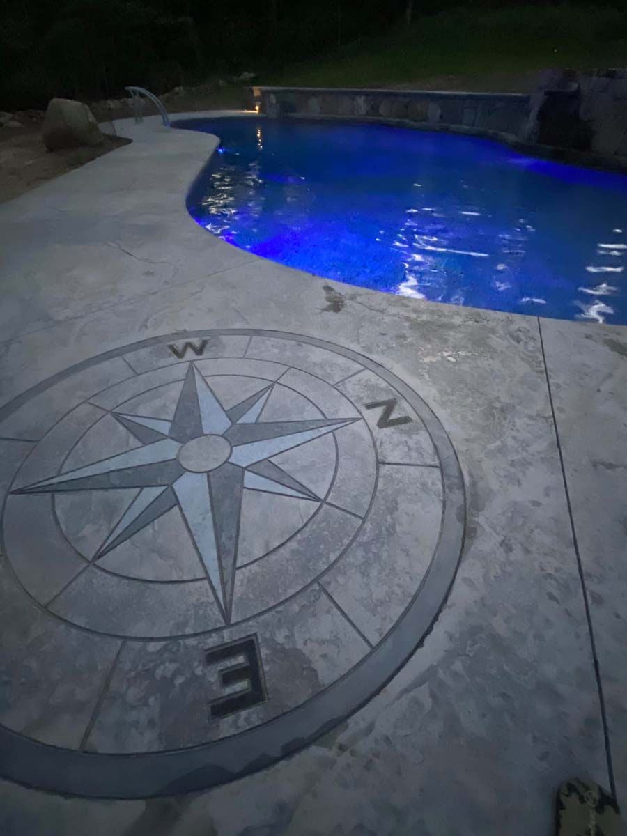 A compass on a concrete patio next to a pool